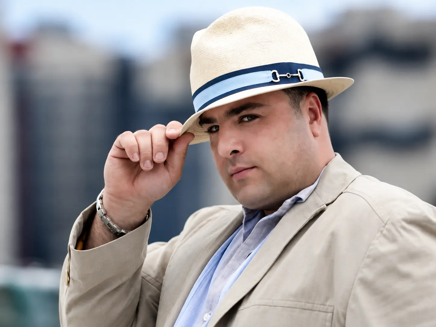 Archival portrait of Tony Stax in a cream hat and jacket, touching the brim.